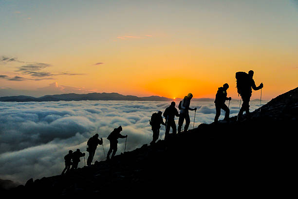 silhouettes of hikers climbing the mountain at sunset.